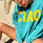A woman wearing a seafoam green crewneck sweatshirt with large yellow 'CIAO' print.

Original design and copyright by first row LA 2026