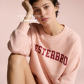 Woman wearing a light pink crewneck sweatshirt with 'VESTERBRO' printed in dark red collegiate letters across the chest.

Original design and copyright by first row LA.