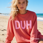 A woman wearing a coral pink sweatshirt with the word 'DUH' printed in light pink across the chest. 

Original design and copyright by first row LA, August 4th 2026.