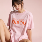 A woman wearing a light pink oversized T-shirt with orangetext reading 'ZOU BISOU BISOU, France 1960' 

Original design and copyright by first row LA.